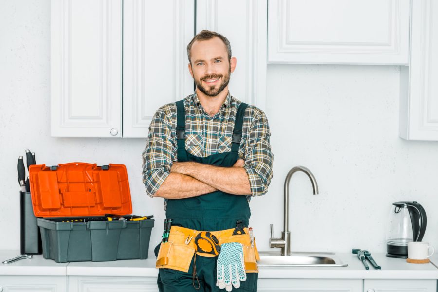 smiling handsome plumber standing with crossed arms and looking at camera in kitchen smiling handsome plumber standing with crossed arms and looking at camera in kitchen